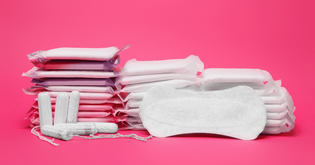 Varios paquetes de compresas apilados, tampones y una compresa abierta sobre un fondo de color rosa intenso.